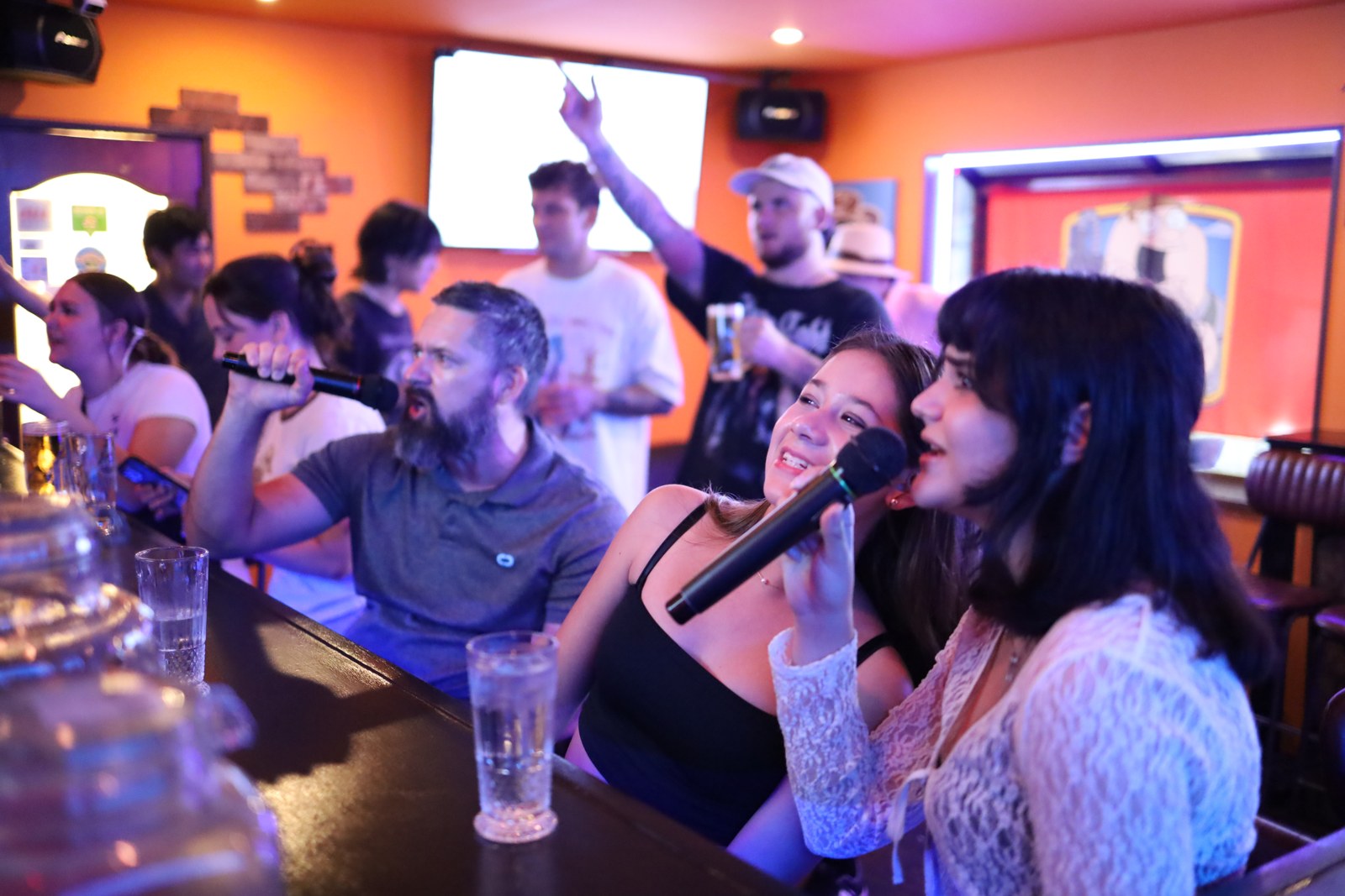 Guests enjoying open-mic karaoke at The Drunken Clam in Osaka, singing with microphones, sharing drinks, and socializing in a lively international bar near Dotonbori.